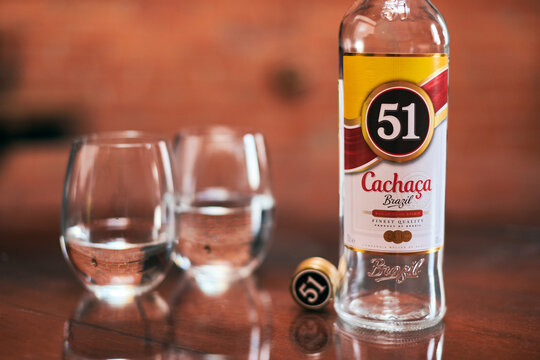 Moscow - 23.11.2019 - Cachaca 51 bottle with two glasses. Brazilian rum. Exotic Brazil strong alcohol drink rom fermented sugarcane juice. Loft apartment background.