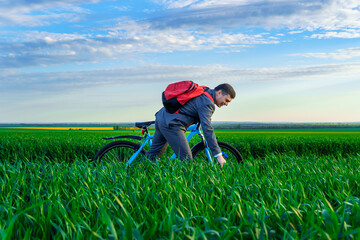 Naklejka na ściany i meble a businessman rides a bicycle with a backpack and a briefcase on a green grassy field, dressed in a business suit, beautiful nature in spring, freelance business concept