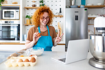 Professional beautiful happy young woman is blogging for her kitchen channel about healthy living in the kitchen of her home and looking on camera on a laptop