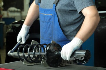 Repair and maintenance of the car at the dealership. An auto mechanic replaces the spring and shock absorber strut of the front suspension of the car.