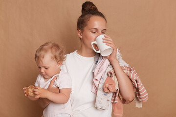 Image of woman with bun hairstyle wearing white T- shirt standing with her little daughter in hands...