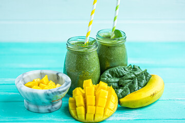 Freshly blended green smoothie with mango and banana in glass jars. Turquoise blue background