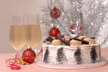 Christmas cake and two glasses of white wine on a Christmas table against decorated silver Christmas tree - 559361446