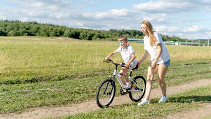 Fototapeta premium loving mother help her cute son ride a bicycle
