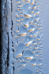 Macro abstract texture background of water droplets and ice forming on an interior glass window pane, with natural designs