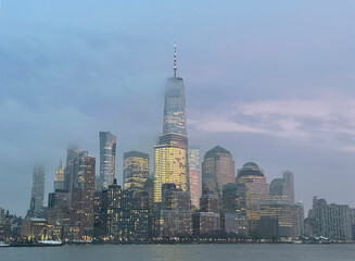 Manhattan financial district in downtown from the Hudson river, with the One Word Observatory as New York's tallest skyscraper on a foggy sunset.