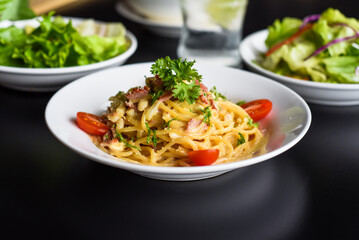 Pasta carbonara with bacon on white plate isolated on black background side view 