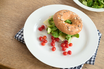 Bagel sandwich with cheese, green lettuce leaves, and cherry tomatoes on a plate - 559372039