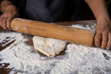 Chef is rolling the dough with the rolling pin on the on the table. Hands close-up.Cooking pasta, bread, spaghetti, khachapuri, food concept