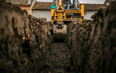 Cropped picture of a backhoe digging soil and making foundation at construction site. - obrazy, fototapety, plakaty