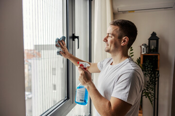 A man is wiping window at home by using detergent and rag.