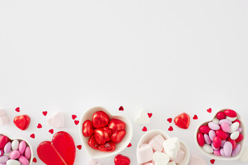 Love Valentines concept. Flat lay photo of heart shaped saucers with sweets candies and lollipops, heart marshmallow on white background with copy space. Sweet Valentines card idea.