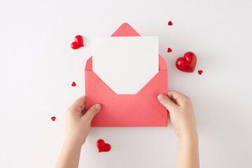 Women day concept. Top view photo of envelope with letter in child hands, red heart shaped baubles...
