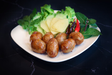 A traditional Thai pork sausage in a white plate . It's a salty with a hint of sourness, it usually grilled or fried, served alongside raw chilis, fresh ginger slices, garlic, and fresh vegetables