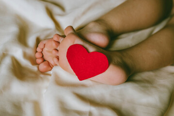 Children's feet and heels with heart on a white bed to Christmas, Valentine's day, Mother's Day. Infant baby is sleeping in his crib. Importance of sleep for babies. Sleep mode babies 3 y.o.