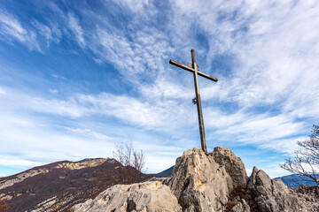 Fototapeta na wymiar Metal religious cross on a mountain peak (Croce di Dos dela Cronela, Monte Altissimo di Nago, Sentiero della Pace) against a blue sky with clouds and copy space. Trentino Alto Adige, Italy, Europe.