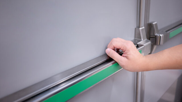 Male hand pushing stainless steel panic bar opening the emergency fire exit door in public building. Fire escape concept