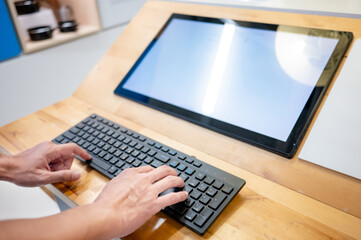 Fototapeta premium Male hand typing on computer keyboard with blank monitor on wooden desk. Computer technology development concept