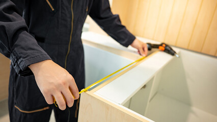 Home renovation or House remodeling concept. Male hand furniture assembler or Interior construction worker man using tape measure installing wooden counter and cabinet of the new kitchen.