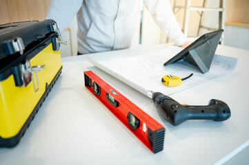 Home renovation or house remodeling. Male Interior worker or furniture assembler man using digital tablet working with architectural drawing and construction tools on countertop of new kitchen.