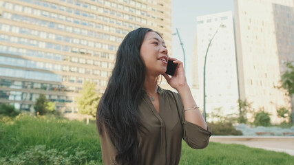 Close up, young smiling girl talking on smartphone while sitting on modern buildings background