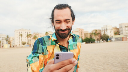 Smiling man sitting and relaxing on the beach with smartphone in his hands