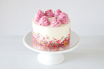 Cake on birthday with pink cream on a white background decorated with colorful sprinkles.