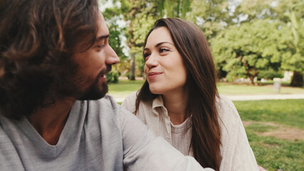 Obraz premium Happy smiling couple talking while sitting on blanket in park. Close-up