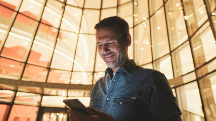 Close up, middle-aged man uses mobile phone in the evening standing next to business center