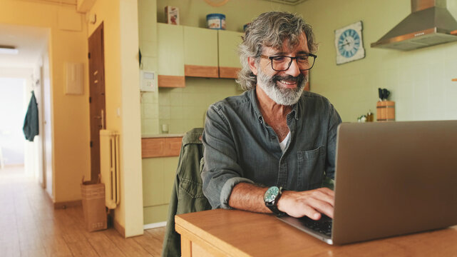 Senior working on laptop sitting in home kitchen