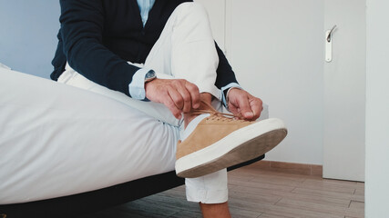 Mature man putting on his casual comfort shoes in front of bed, tying his shoelace