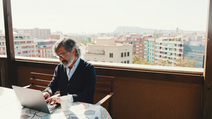 Middle-aged man working on laptop while with coffee sitting on balcony