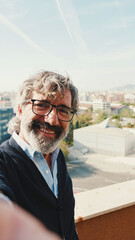 Close-up of mature man taking selfie while standing on balcony, looks at camera