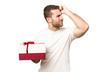 Young handsome blonde man holding a gift over isolated chroma key background having doubts and with confuse face expression