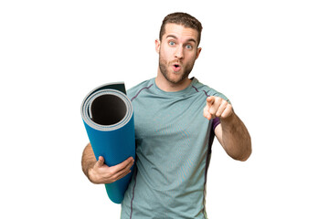 Young sport man going to yoga classes while holding a mat over isolated chroma key background surprised and pointing front