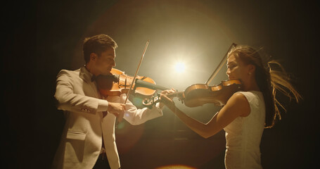 Duet of two professional violin players having a solo together, performing on stage during concert,...