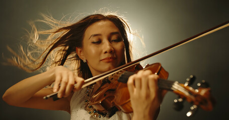 Professional female violin player performing an amazing solo during concert, spotted by light on...