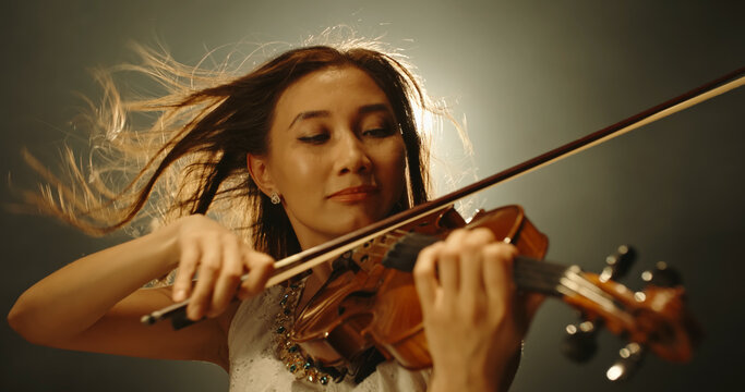 Professional female violin player performing an amazing solo during concert, spotted by light on smoked black background 