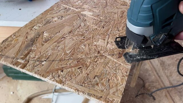 Woodworker cutting a piece of OSB board in arched forme with a jigsaw.