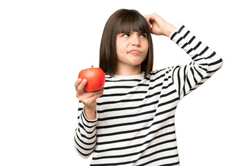 Little girl with an apple over isolated chroma key background having doubts and with confuse face...