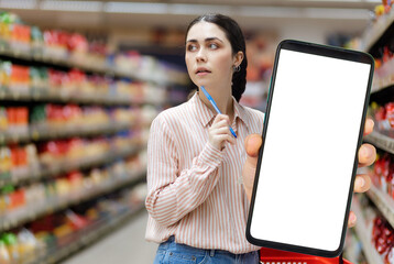 Sales in supermarket. Portrait of young Caucasian pretty woman shows big smartphone with white screen and mock up and choice. Copy space. Concept of discount apps