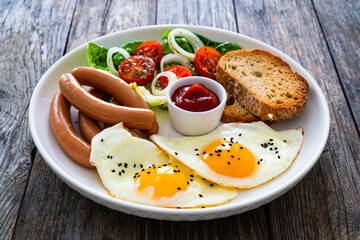 Breakfast - sunny side up egg, boiled sausages and vegetables served on wooden table
