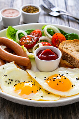 Breakfast - sunny side up egg, boiled sausages and vegetables served on wooden table
