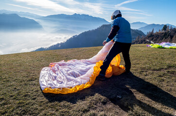 Man on a grassy slope prepare the glider for paragliding from Vetriolo Terme, Trento province - Trentino Alto Adige - Paragliding school - Italy