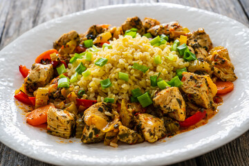 Fried chicken nuggets, bulgur groats, carrots and red pepper on wooden background
