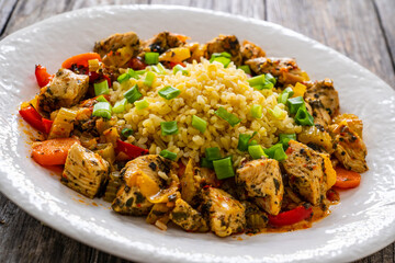 Fried chicken nuggets, bulgur groats, carrots and red pepper on wooden background
