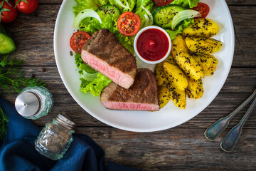 Fried beef sirloin with  potatoes and vegetables on wooden table

