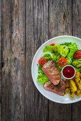 Fried beef sirloin with  potatoes and vegetables on wooden table
