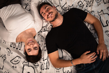 Beautiful couple are lying on the bed and looking at the camera. Young couple photographed from above. - 559415407