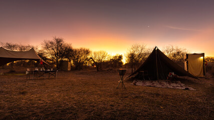 Fototapeta na wymiar Camping in the wilderness. A pitched tent under the glowing sunset sky, Laikipia, Kenya. 